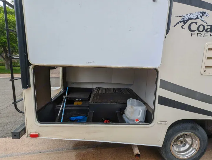 Open storage in an RV rental reveals camping essentials: a water jug, mats, and tools.. Forest River Coachmen Freelander 2018