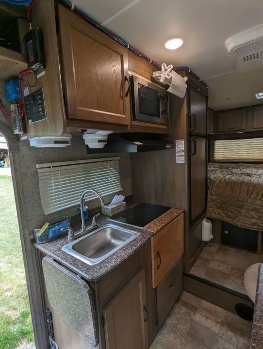 Compact RV rental kitchen/galley with sink, microwave, fridge, and sleeping area beyond, showcasing full amenities for travel.. Forest River Coachmen Freelander 2018