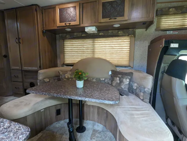 RV rental interior: cozy U-shaped dinette with table, overhead cabinets, and window blinds, perfect for dining & relaxation.. Forest River Coachmen Freelander 2018