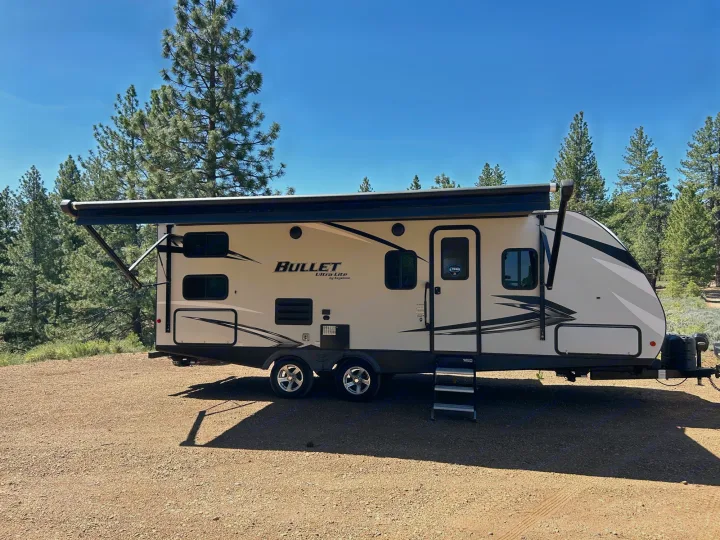 RV rental parked in sunny nature setting with pine trees. Perfect for outdoor adventure.. Keystone RV Bullet Ultra Lite 2021