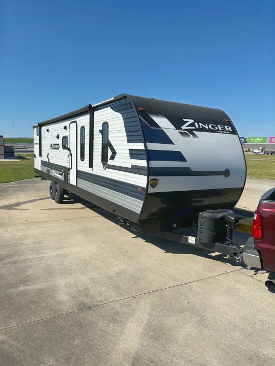 White "Zinger" travel trailer RV rental, hitched to a red truck, parked on a concrete lot under a clear blue sky.. Crossroads RV Zinger 2022