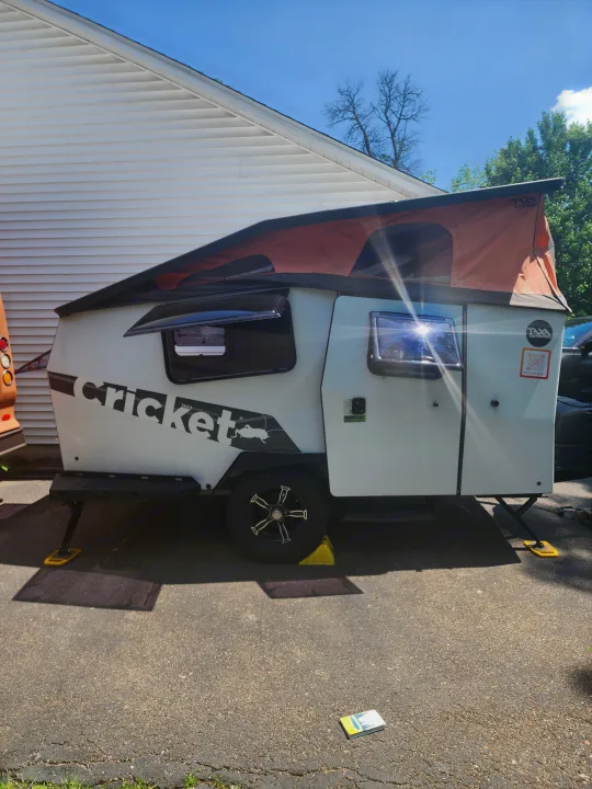 Compact Taxa Outdoors Cricket RV rental with pop-up roof, parked on pavement. A unique travel trailer for adventure.. TAXA TAXA Trailer 2021