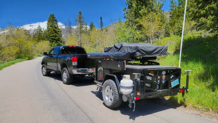 This RV rental setup, featuring a pickup truck towing an overlanding trailer with a rooftop tent, offers mountain adventures.. Insane Custom Trailers "Squatchy" 2022