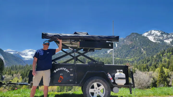 Man beside his 'Squatchy' off-road trailer featuring a Rhino-Rack rooftop tent, ideal for an RV rental mountain adventure.. Insane Custom Trailers "Squatchy" 2022