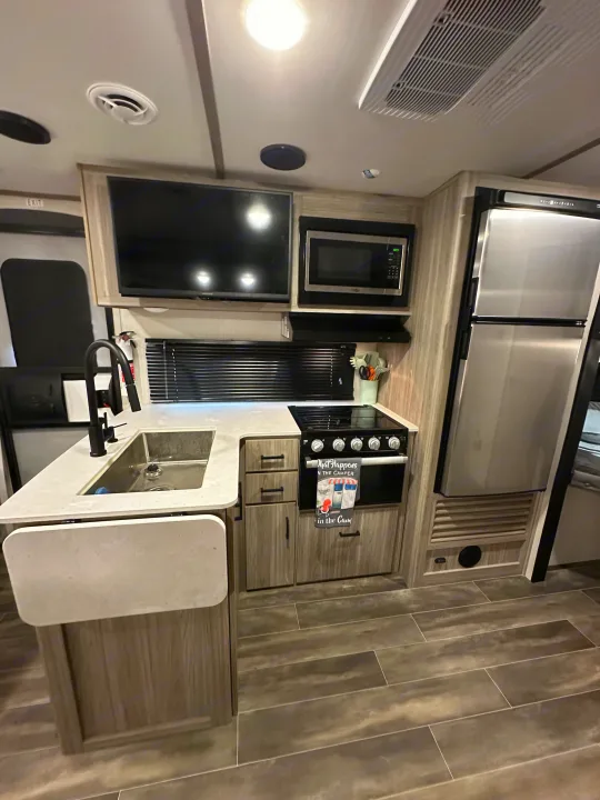 A well-appointed RV rental kitchen with a sink, stove, microwave, and fridge, efficiently designed for comfortable living.. Keystone RV Passport SL 2022