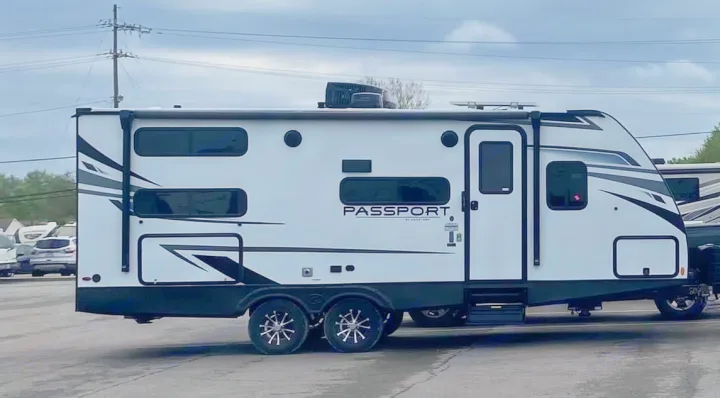 White Passport travel trailer, a perfect RV rental option, featuring black accents, dual axles, and a rooftop AC unit.. Keystone RV Passport SL 2022