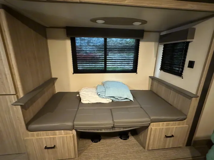 RV rental interior: spacious dinette with gray cushions, convertible bed, window blinds, and under-seat storage.. Keystone RV Passport SL 2022