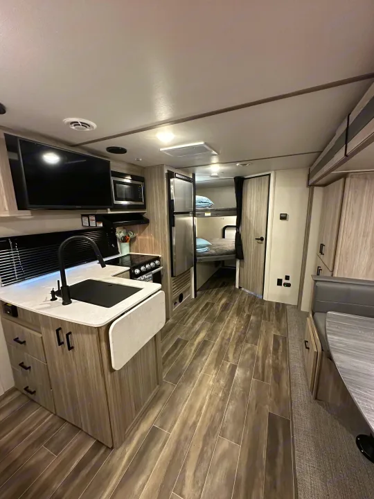 Modern RV rental interior featuring a kitchen with sink and stove, plus bunk beds and a dinette area.. Keystone RV Passport SL 2022