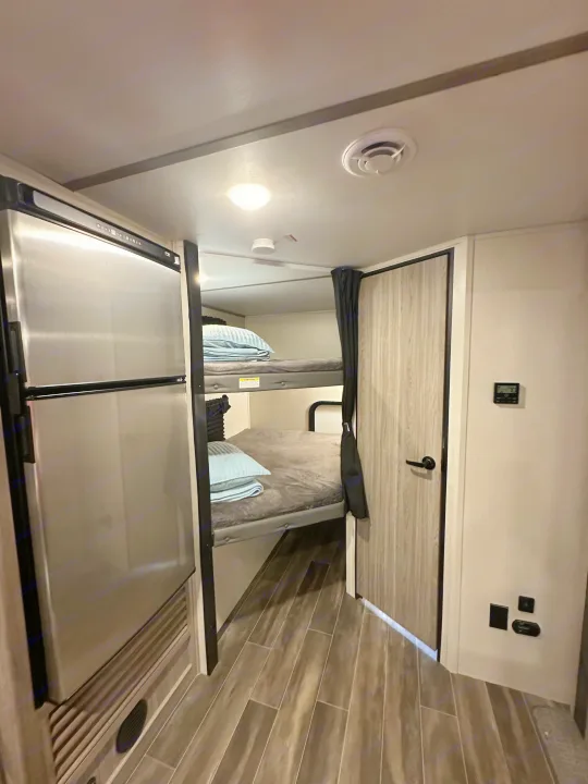 RV rental interior featuring comfortable bunk beds next to a stainless steel refrigerator, ideal for mobile living.. Keystone RV Passport SL 2022