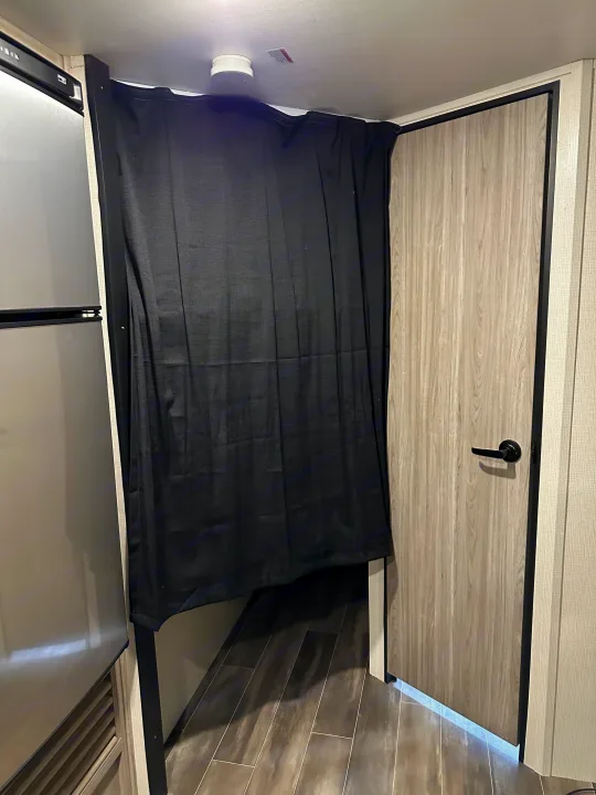 RV rental: A black privacy curtain separates living spaces, next to a fridge and a wood-look door.. Keystone RV Passport SL 2022
