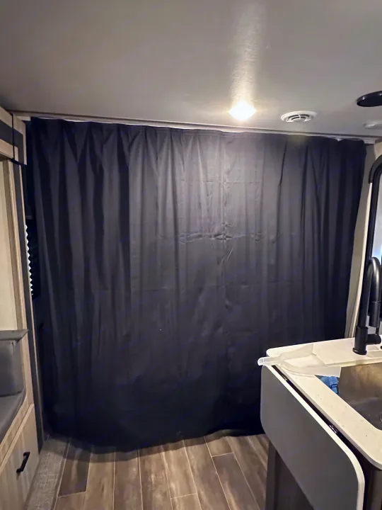 RV rental interior: blackout curtain for privacy, with sink, faucet, and durable wood-look flooring visible.. Keystone RV Passport SL 2022