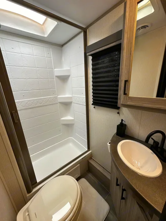RV rental bathroom interior featuring a bright shower with skylight, toilet, and modern sink vanity for comfort.. Keystone RV Passport SL 2022