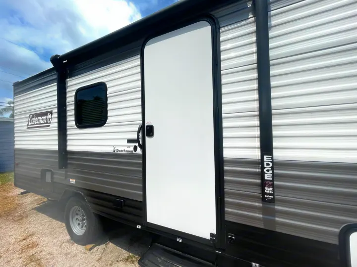 Open door on a Coleman Dutchmen travel trailer, showcasing its white and gray exterior, ideal for rv rental.. Dutchmen Coleman Lantern LT 2023