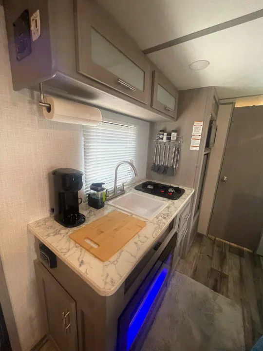 Compact RV rental kitchen with sink, stove, coffee maker, and modern cabinets.. Dutchmen Coleman Lantern LT 2023