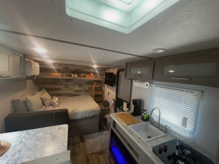 This RV rental's inviting interior features a cozy bedroom with wood accent wall, bright kitchenette, and living space.. Dutchmen Coleman Lantern LT 2023