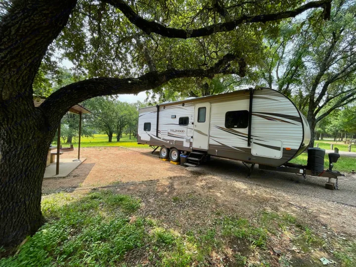 RV rental parked at a shaded campsite, surrounded by trees and nature, perfect for an outdoor camping getaway.. Forest River Wildwood 2016