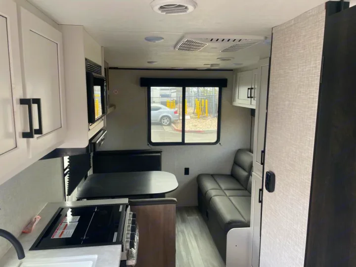 RV rental interior: A compact kitchen with stovetop, microwave, dinette, and sofa provide a functional living space.. Jayco Jay Flight SLX 2024