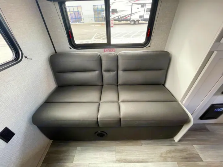 View inside an RV rental: Grey upholstered dinette seating, wood-grain floor, and a window displaying an "EXIT/SORTIE" sign.. Jayco Jay Flight SLX 2024