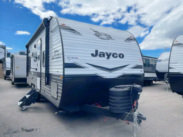 A gray and black Jayco travel trailer RV, ready for rental adventures, parked outdoors under a blue sky.. Jayco Jay Flight SLX 2024