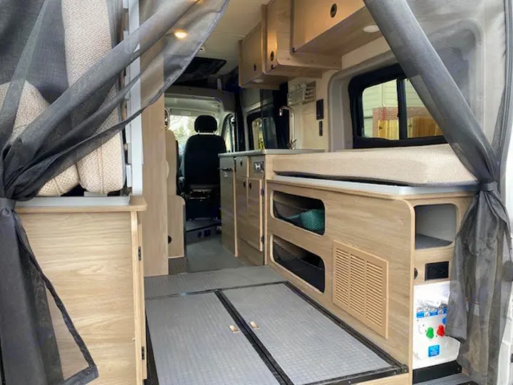 Modern RV rental interior showing a compact living space, complete with a bed/bench, storage, and a small sink area.. Winnebago Solis 2021