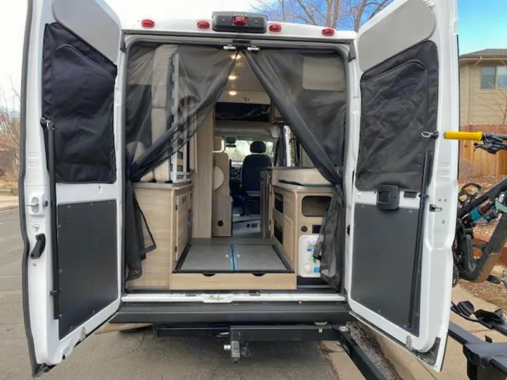 Rear view of a modern RV rental camper van, doors open, revealing its compact, functional interior and a bike rack. Perfect for travel.. Winnebago Solis 2021