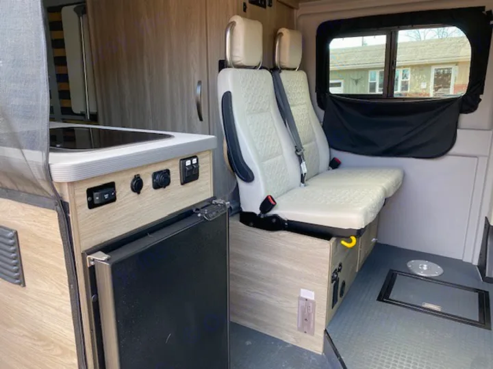 RV rental van interior with compact kitchen, passenger seating, and rear windows, perfect for travel adventures.. Winnebago Solis 2021