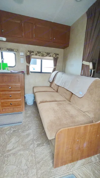 Cozy RV rental interior featuring a tan couch, wooden cabinets, a small kitchen area with a sink, and windows with curtains.. Jayco Jay Flight Swift 2012