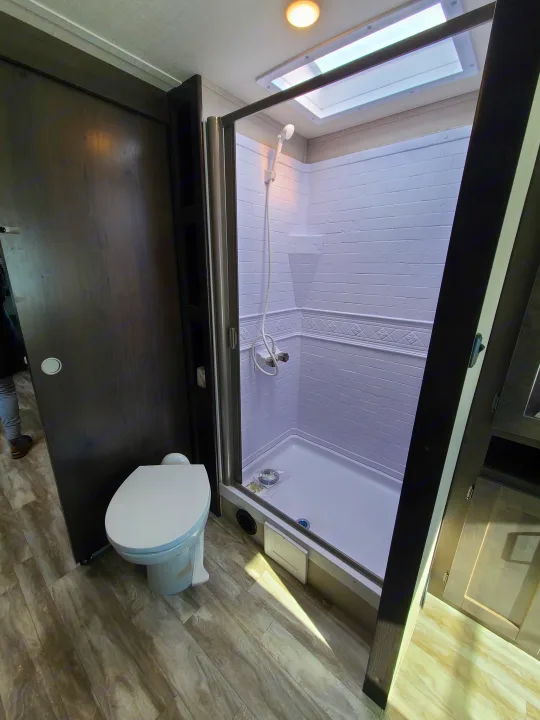 RV rental bathroom: modern toilet, bright shower with skylight, and wood-look flooring.. Grand Design Transcend Xplor 2022