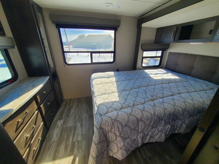 Explore this cozy RV rental bedroom featuring a comfy bed with modern patterned comforter, built-in storage, and bright windows.. Grand Design Transcend Xplor 2022
