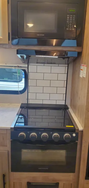 RV rental kitchen featuring Greystone microwave, stovetop, and oven, with tile backsplash and countertop.. Gulf Stream Trailmaster 2023