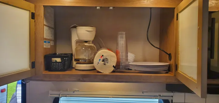 An RV rental's organized kitchen cabinet, prepared for guests with a coffee maker, plates, cups, and paper towels.. Gulf Stream Trailmaster 2023