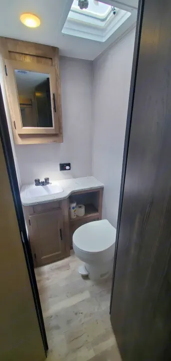 A modern, compact RV rental bathroom with a vanity, sink, mirror, toilet, and overhead skylight providing natural light.. Gulf Stream Trailmaster 2023