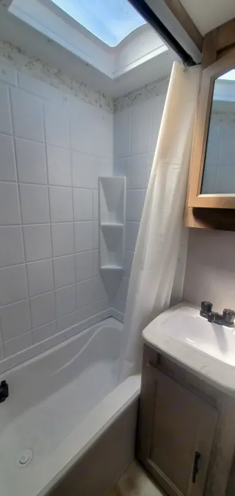 Bright RV rental bathroom featuring a white bathtub, shower with built-in shelves, and a vanity with sink.. Gulf Stream Trailmaster 2023