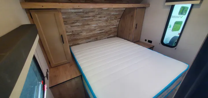 Bright RV rental bedroom showcasing a plush white mattress, wood-look headboard, and built-in storage.. Gulf Stream Trailmaster 2023