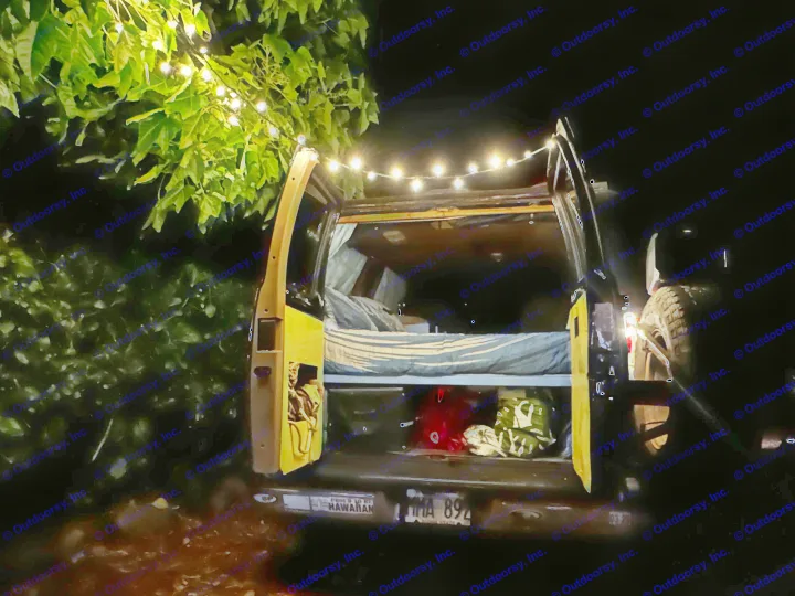 Cozy rv rental at night: open back of a camper van with bed and string lights draped over doors and a tree.. Dodge 1500 1999