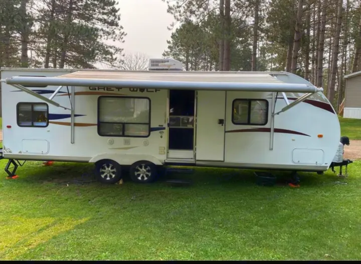 This Grey Wolf travel trailer, great for an RV rental, is set up on a grassy lot with its awning extended.. Forest River Cherokee Grey Wolf 2012