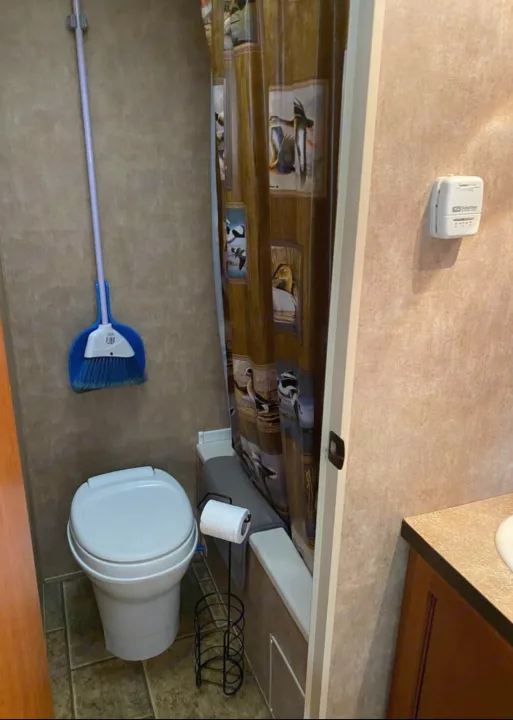 Inside a practical RV rental bathroom: compact toilet, shower with duck curtain, and a wall-mounted thermostat. Essential amenities for travel.. Forest River Cherokee Grey Wolf 2012