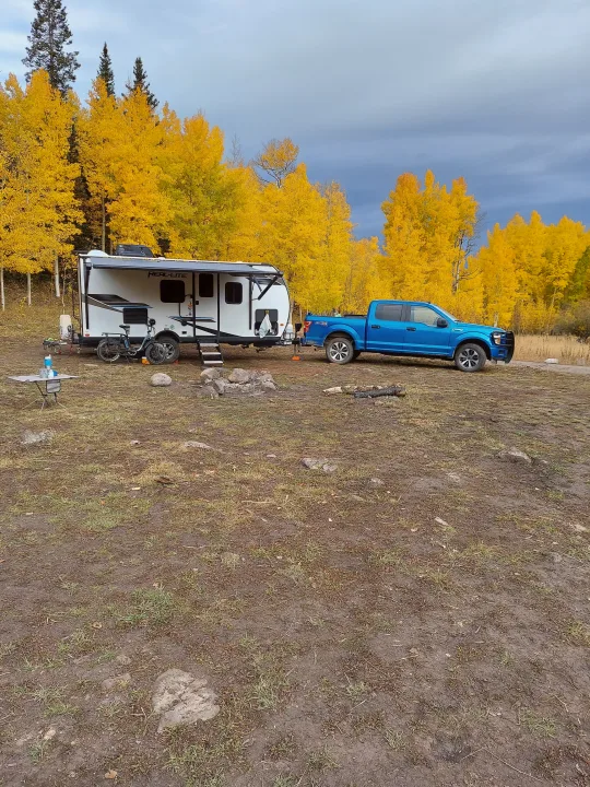 RV rental & blue truck camping among brilliant golden aspens under a cloudy sky. Autumn adventure setup.. Forest River Palomino Real-Lite Mini 2021