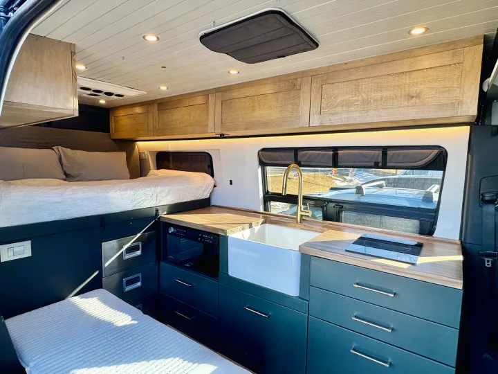 Stylish RV rental interior with a comfortable bed, functional kitchenette featuring a sink, cooktop, and ample storage.. Mercedes-Benz Sprinter 2021