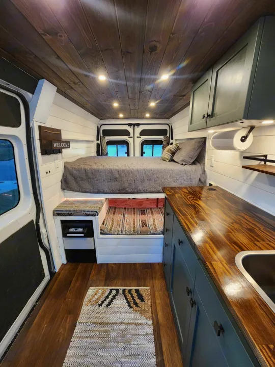 Detailed RV rental interior: raised bed, kitchen, wood ceiling, and white walls in a modern camper van conversion.. Dodge 1500 2014