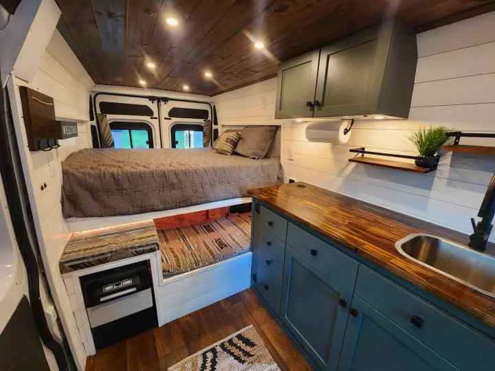 Interior of a custom camper van RV rental, showing a cozy bed, modern kitchen, and warm wood ceiling. Ideal for road trips!. Dodge 1500 2014