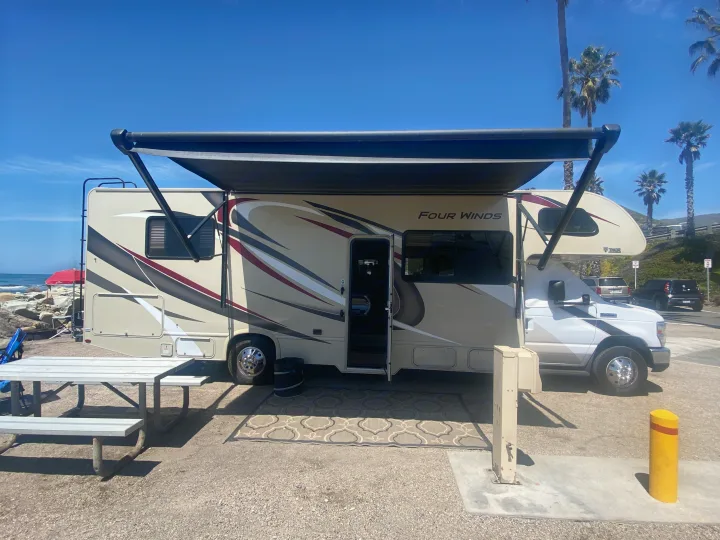 This RV rental is perfectly set up for beachside camping, featuring a large RV with an extended awning, a picnic table, and ocean views.. Thor Four Winds 2020