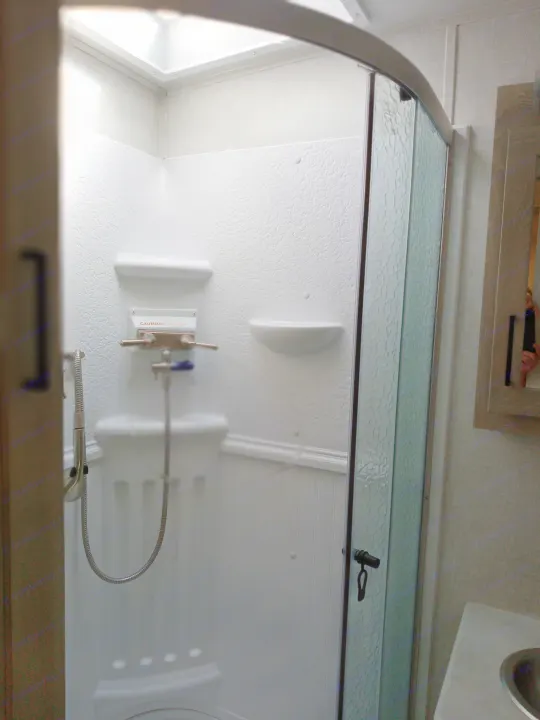 Inside an RV rental shower: textured walls, practical shelving, and a translucent sliding door with showerhead.. Forest River Rockwood Signature 2021