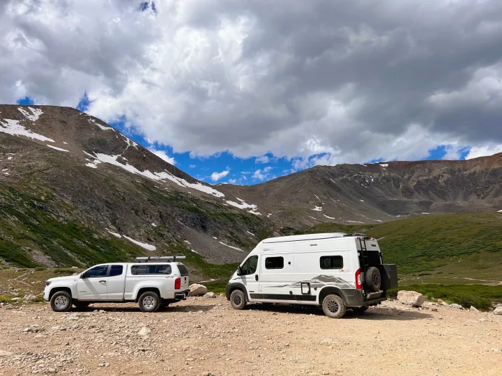 An RV rental camper van & pickup truck explore a rugged mountain road with snow. Ideal for outdoor adventures!. Winnebago Solis 2023