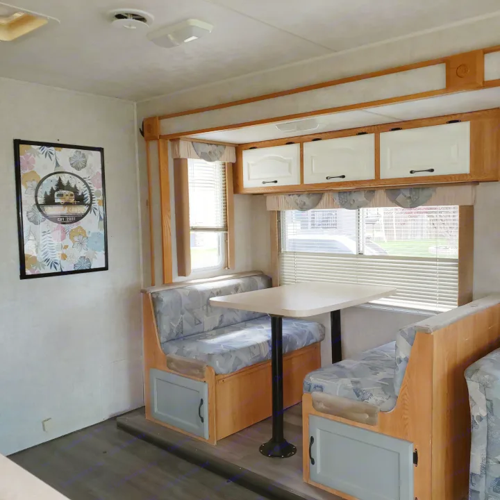 RV rental interior featuring a cozy dinette with patterned seating, a table, and light wood overhead storage cabinets.. Damon Corporation Daybreak 2002