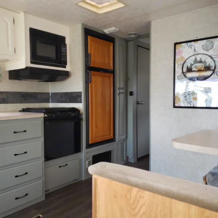 This RV rental kitchen has light gray cabinets, black microwave/stove, and a wood refrigerator, creating a cozy living space.. Damon Corporation Daybreak 2002