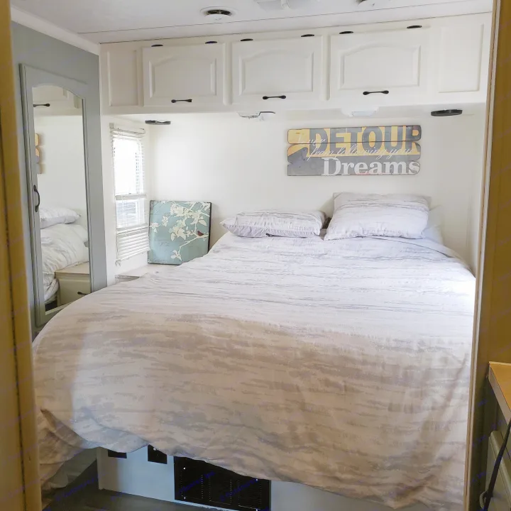 Cozy RV rental bedroom featuring patterned bedding, overhead cabinets, a side mirror, and a window with blinds for travel comfort.. Damon Corporation Daybreak 2002