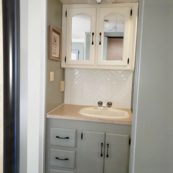 This RV rental shows a refreshed bathroom with a light grey vanity, white chevron backsplash, and matching white upper cabinets.. Damon Corporation Daybreak 2002
