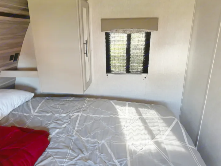 Cozy RV rental bedroom with a grey patterned bed, a small window with blinds, and a light-colored storage cabinet.. Crossroads RV Cruiser Aire 2021