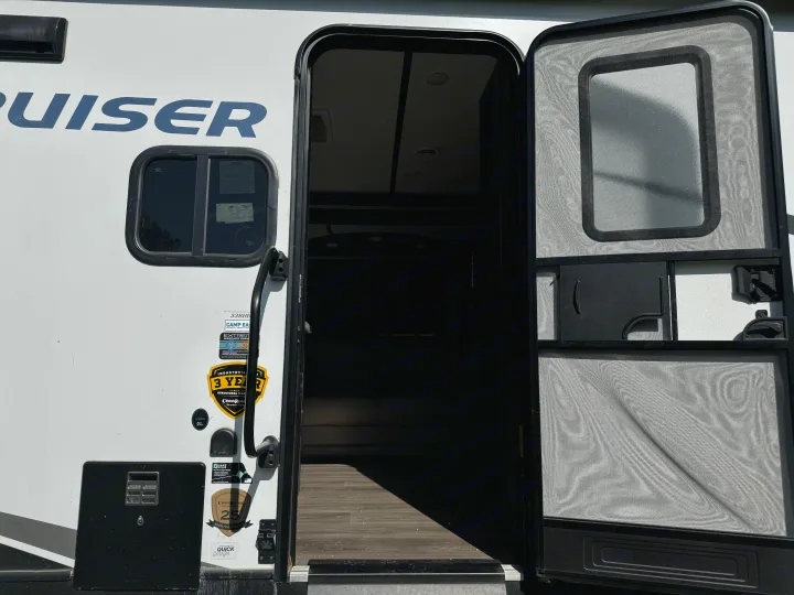 White RV rental with its main door and screen door open, revealing the dark interior and part of the floor.. Crossroads RV Cruiser Aire 2021